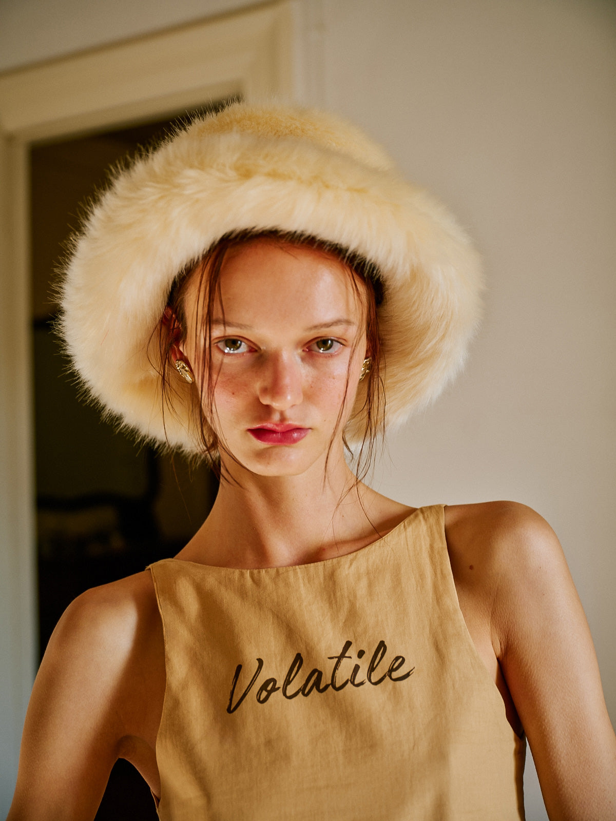 WAYT Studio imzalı Polunin suni kürk şapka, modelin üzerinde dikkat çekici bir görünüm sunuyor. Kremsi tonuyla sıcaklık hissi veren bu geniş kenarlı şapka, zarif detayları ve retro havasıyla dikkat çekiyor. Gün ışığında çekilmiş portre stilinde moda görseli.